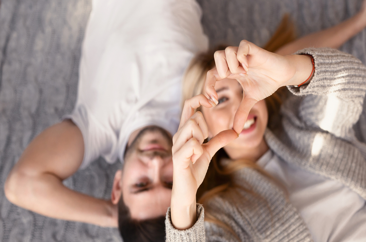 Young man and his girlfriend making heart with her hands indoors, overhead view.